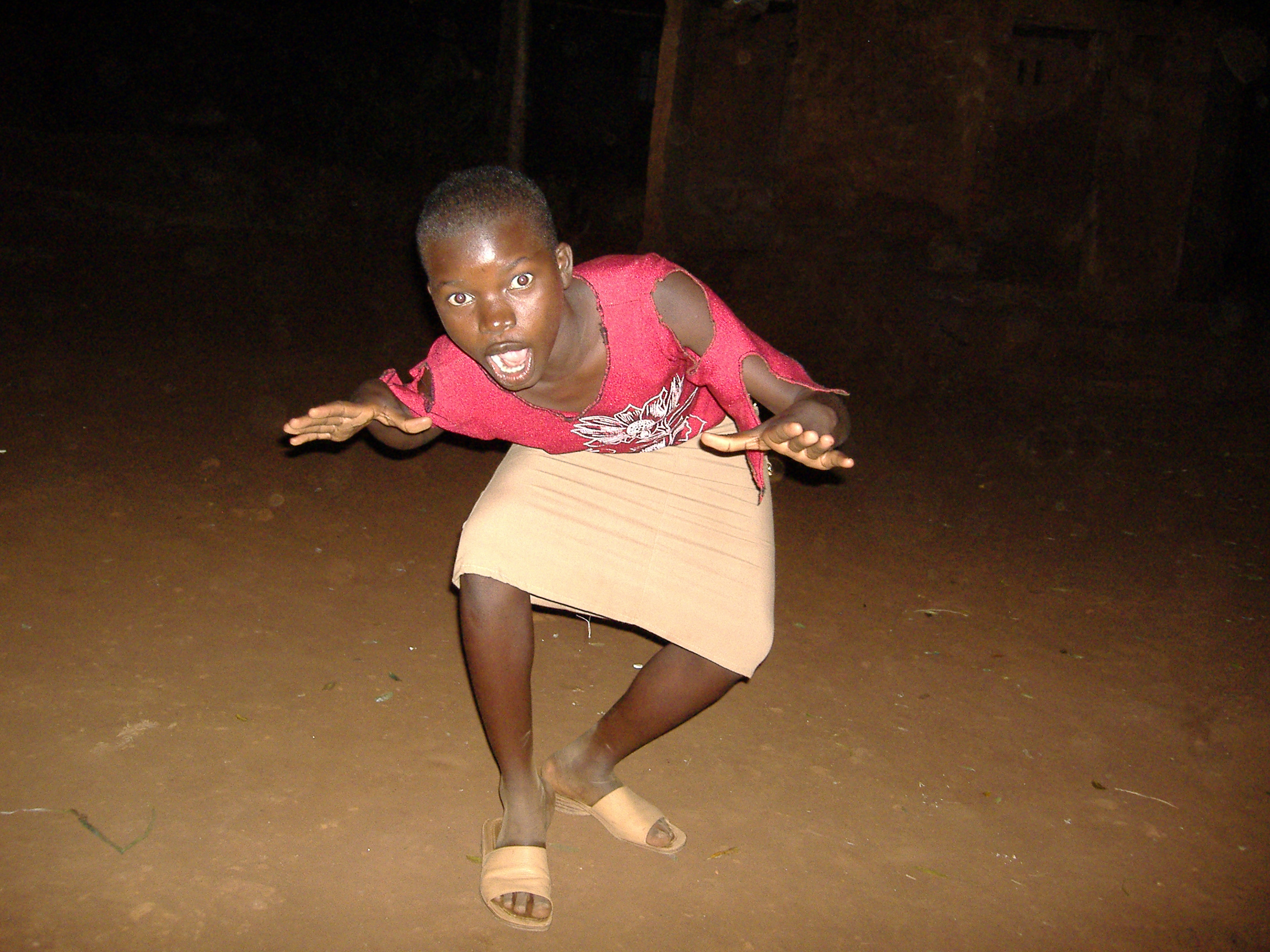 A crowd of Malawi men watch a masked man dance the Gulewamkulu.
